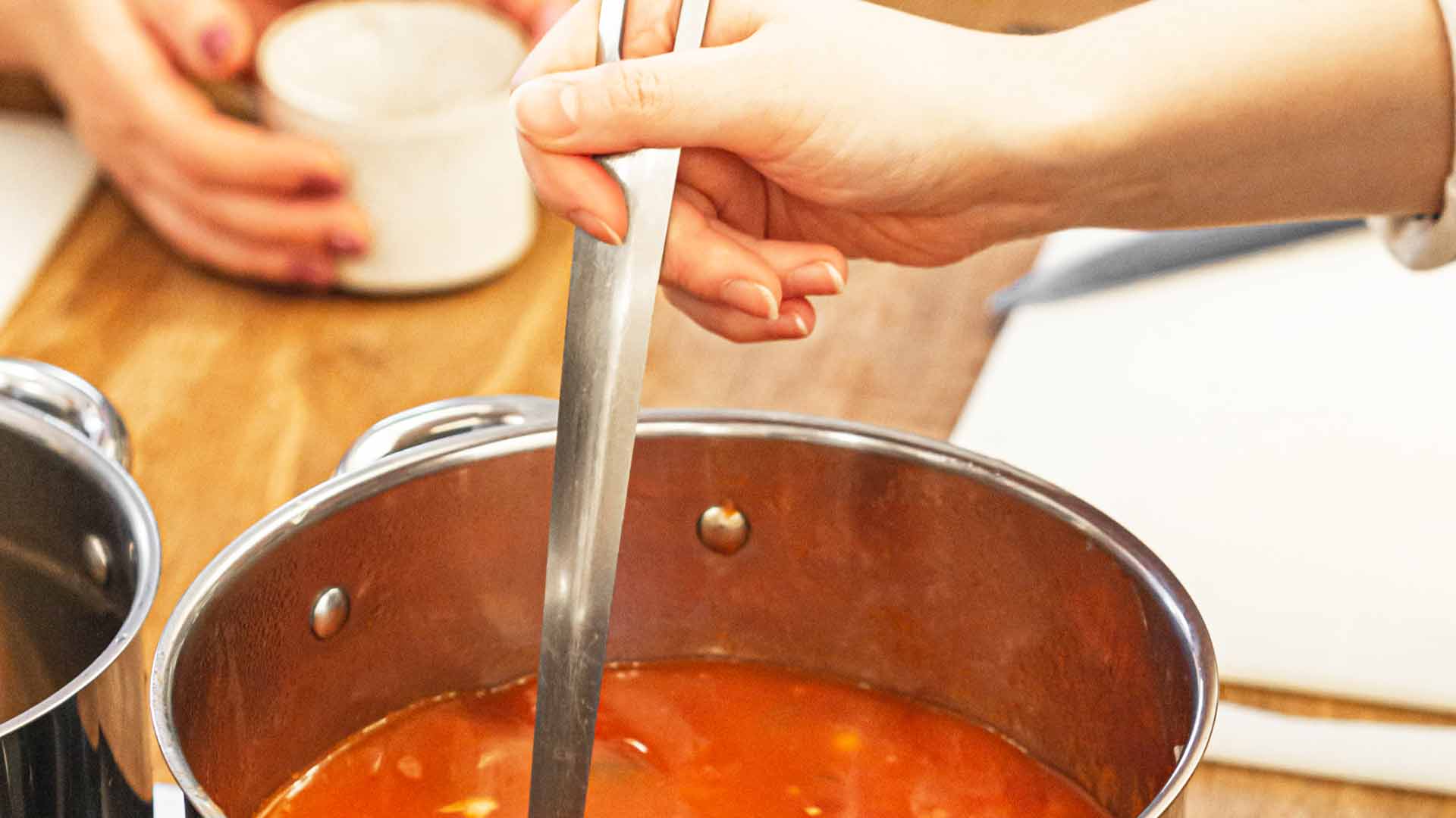 Eine Hand rührt mit einer Kelle eine rote Soljanka in einem großen Edelstahltopf um.